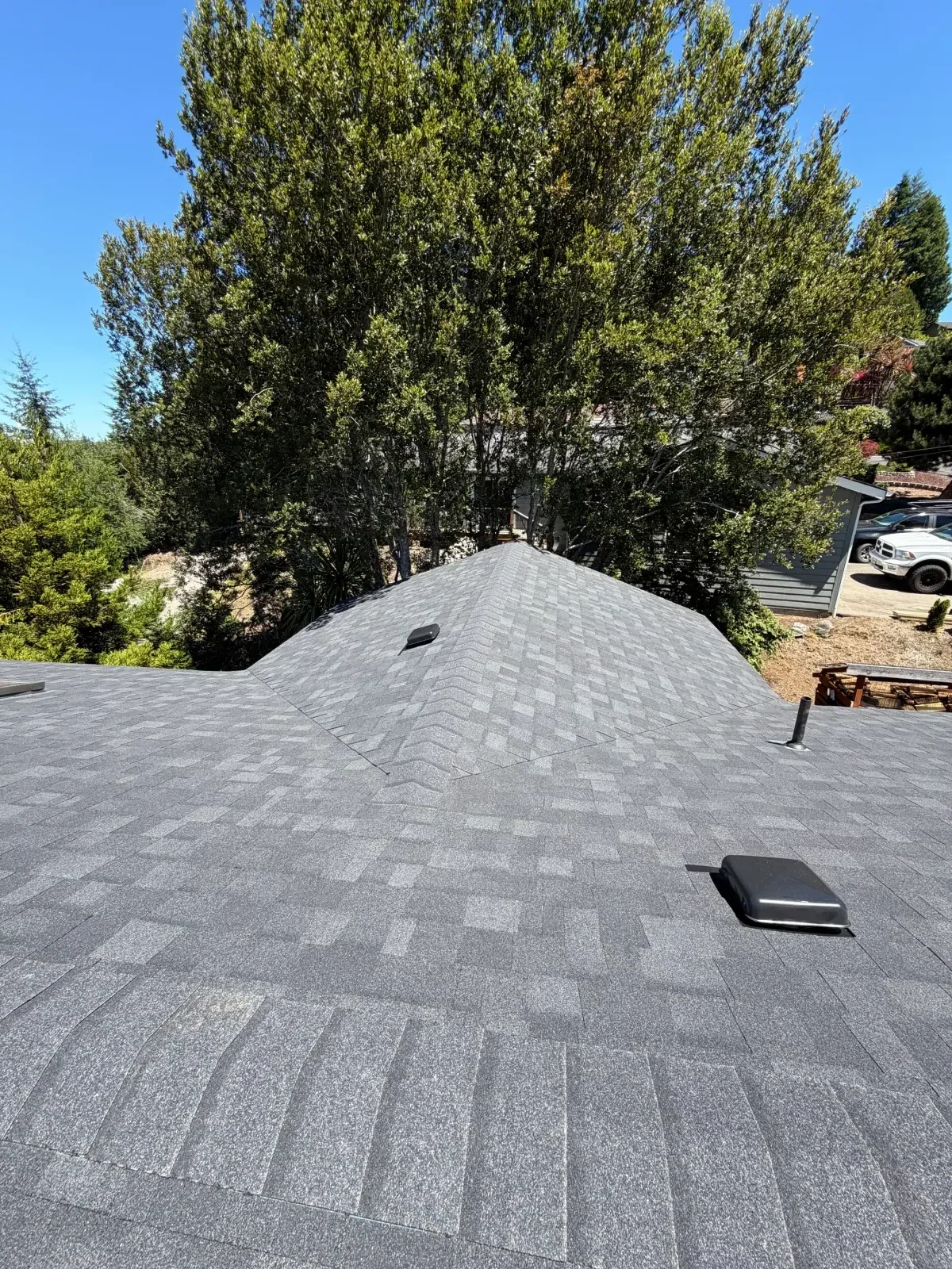 Gray architectural asphalt shingle roof with black vent pipe boot and box roof vent, ridge and hip lines visible