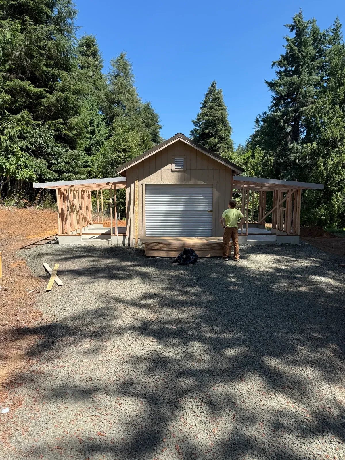 Small outbuilding under construction with tan lap siding, corrugated metal roll-up door, and exposed wood framing