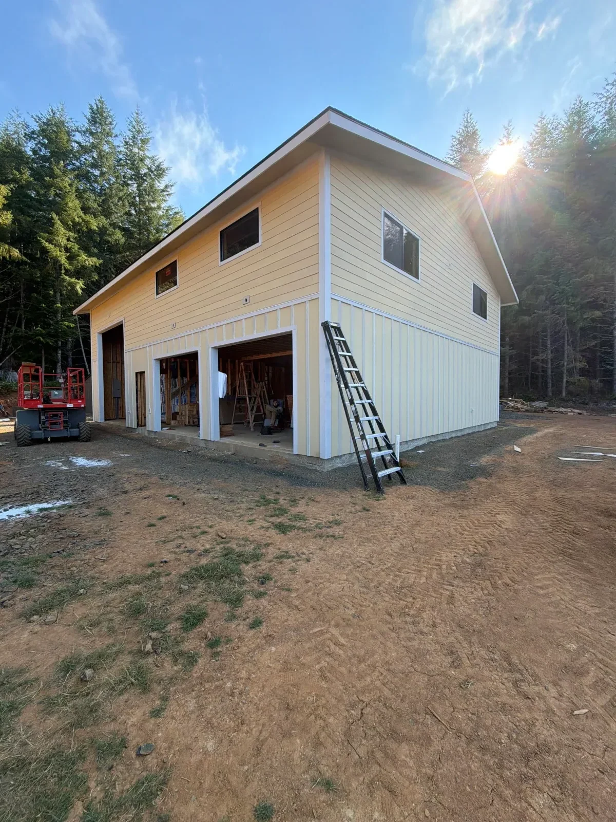 Two-story building with tan vertical siding, white trim, gable roof, and open framed bays under construction